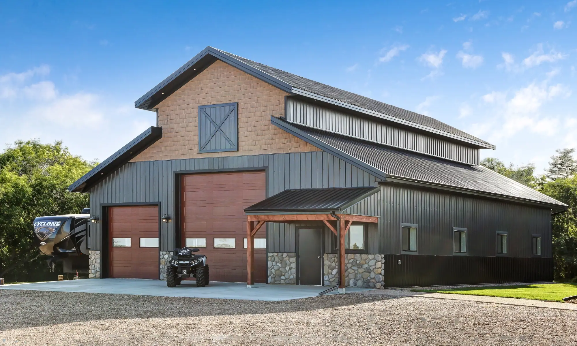 Premium custom pole barn building with monitor-style roof, stone accents, garage doors, and covered entrance for an elevated appearance.