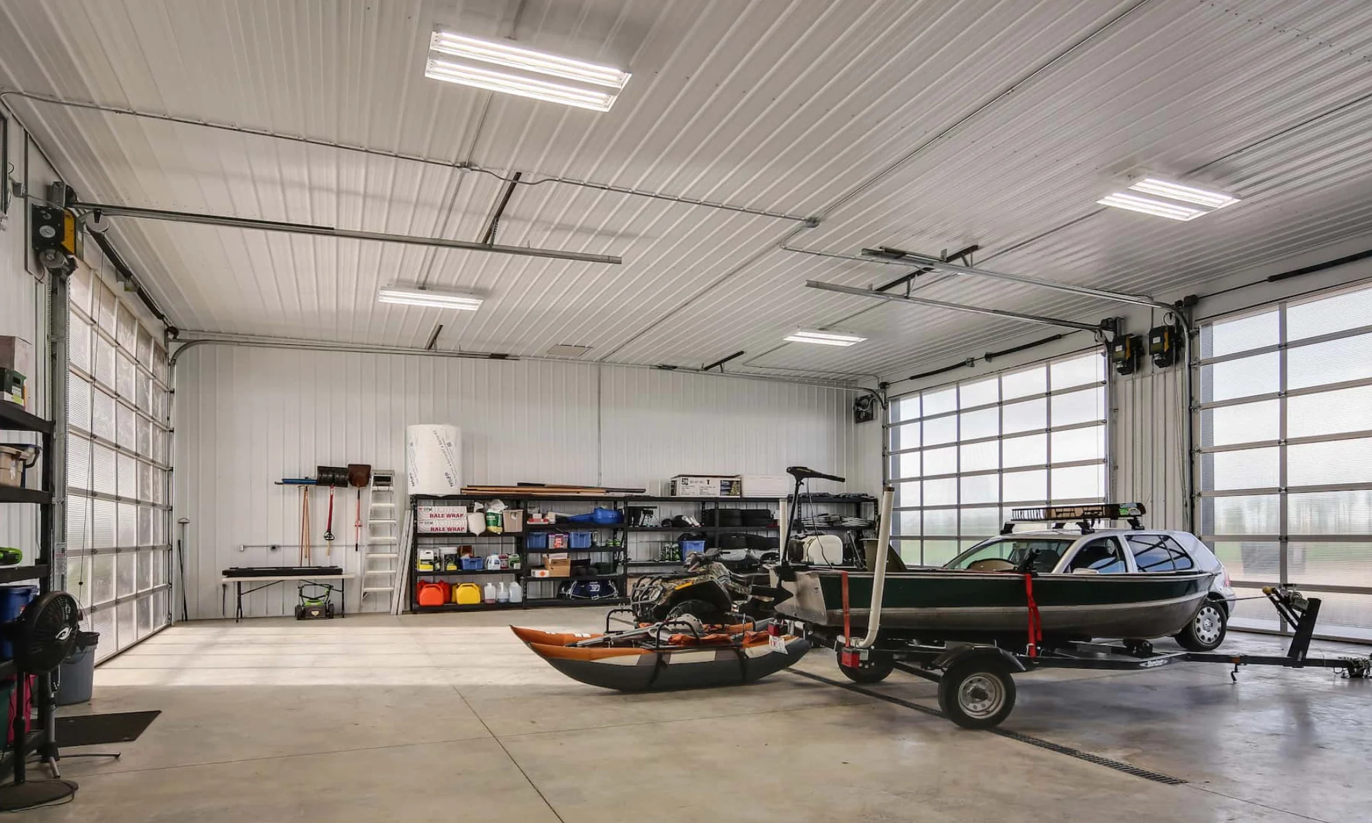 Interior of a pole barn building garage with storage capacity for a boat and other vehicles, brightly lit by an overhead door with glass panels.