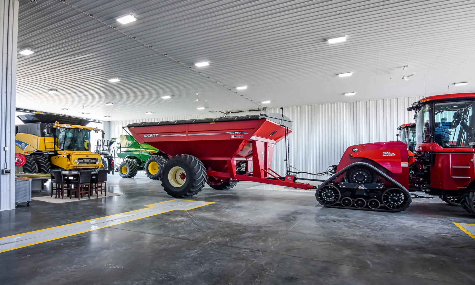 Interior of a fully finished farm building used as a workshop and storage for large tractors, grain carts, and other machinery.