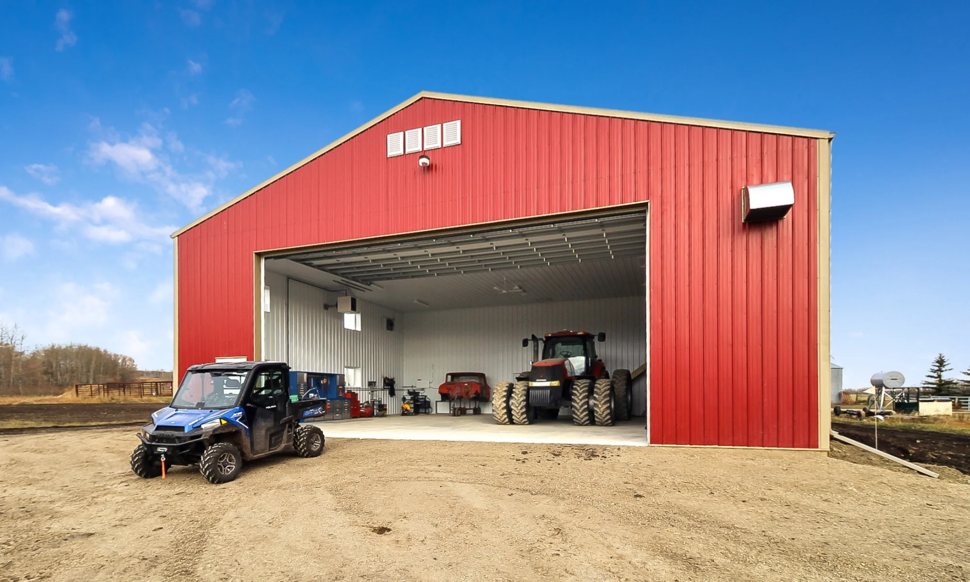 Red metal farm building with overhead door and finished interior to store tools and store or maintain tractors.