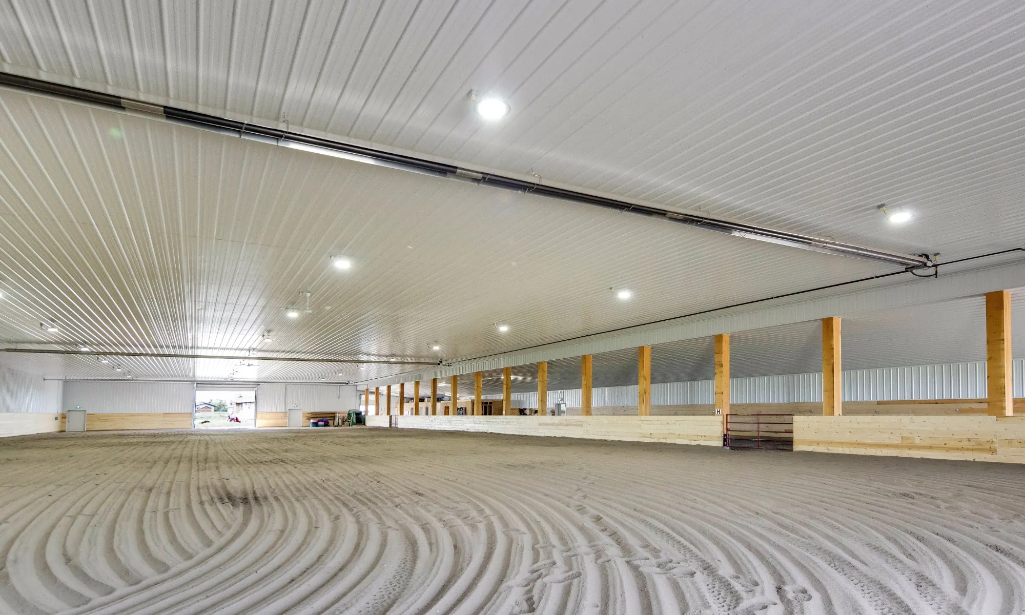 Spacious indoor riding arena inside a premium post frame horse shelter with groomed footing and durable, eye-catching finishes.