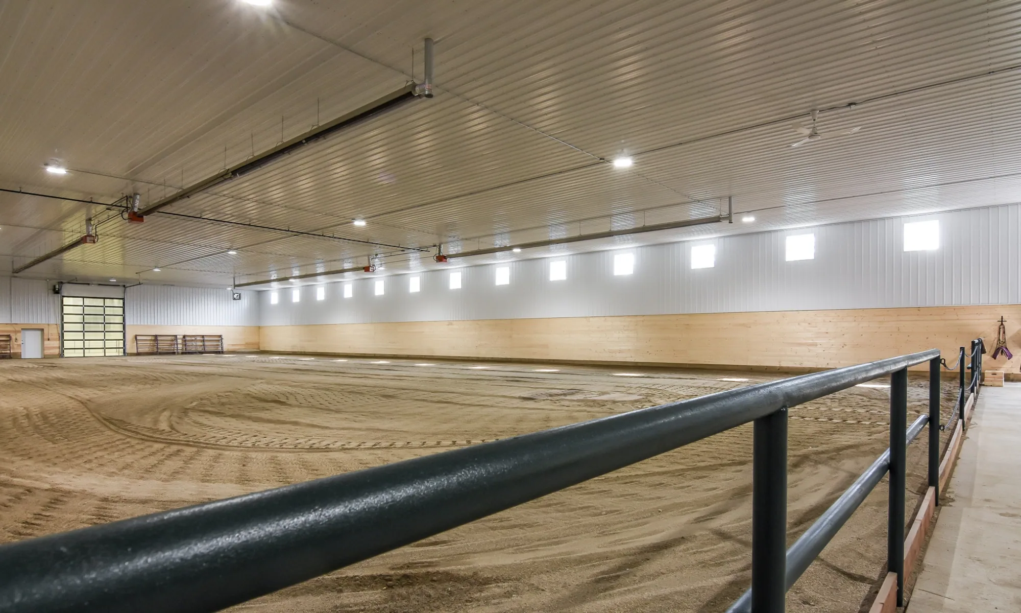 Interior of a horse shelter that includes a manicured riding arena that is bright and spacious.