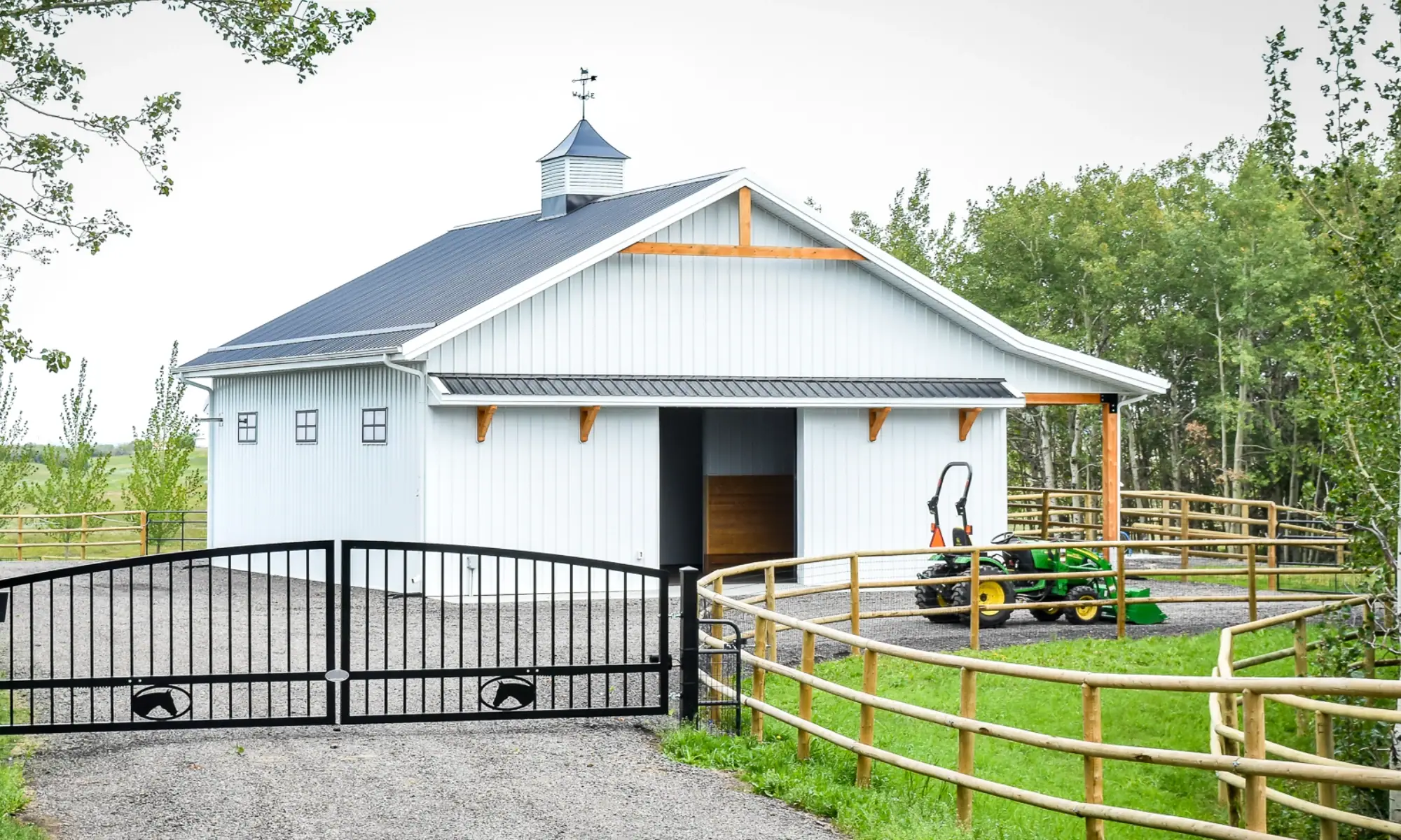 Custom-built horse shelter with timber accents, cupola, and fenced entry in a rural setting.