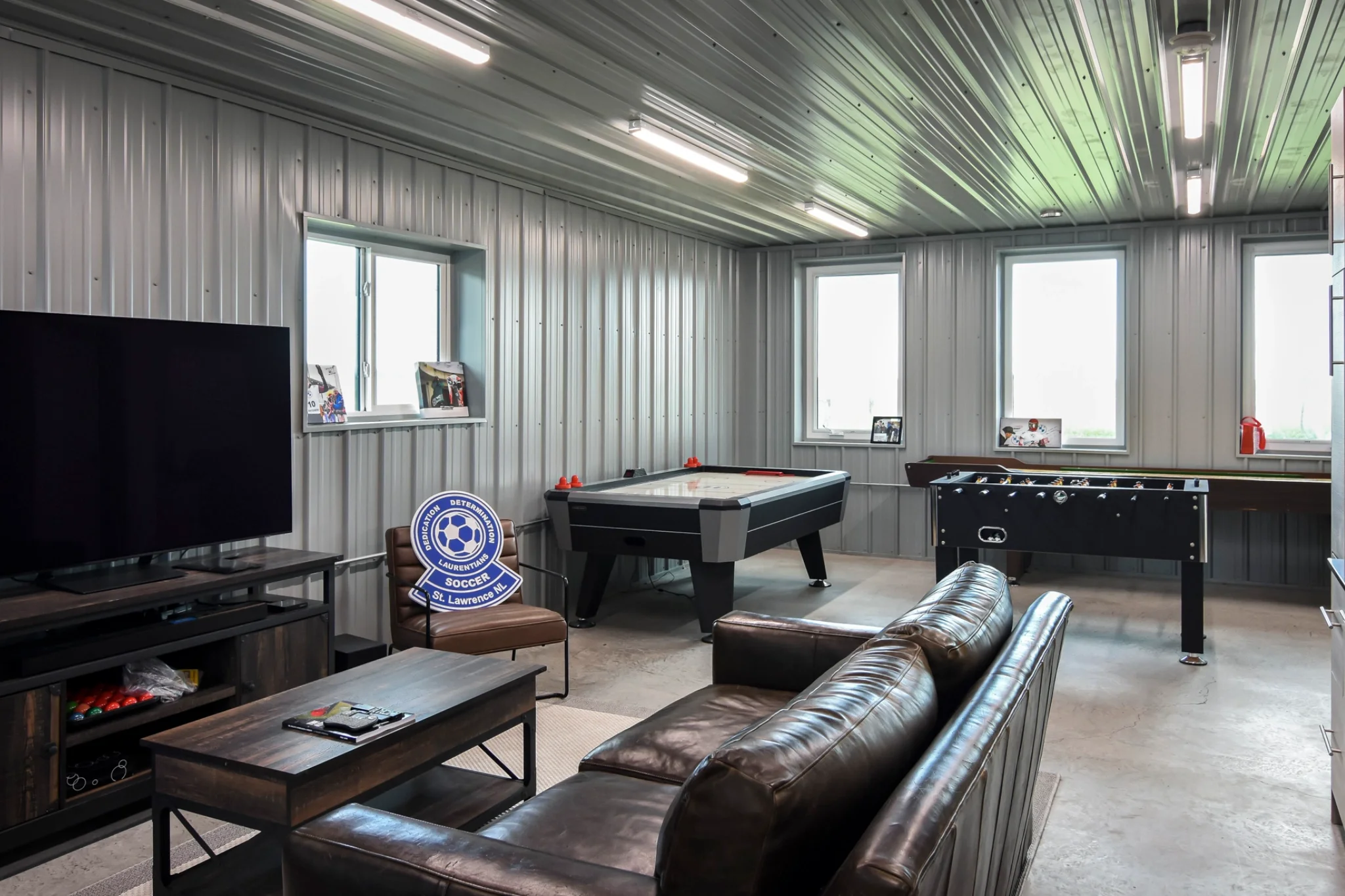 The lounge area inside a post frame building has a couch, tv, and games for relaxation and recreation.