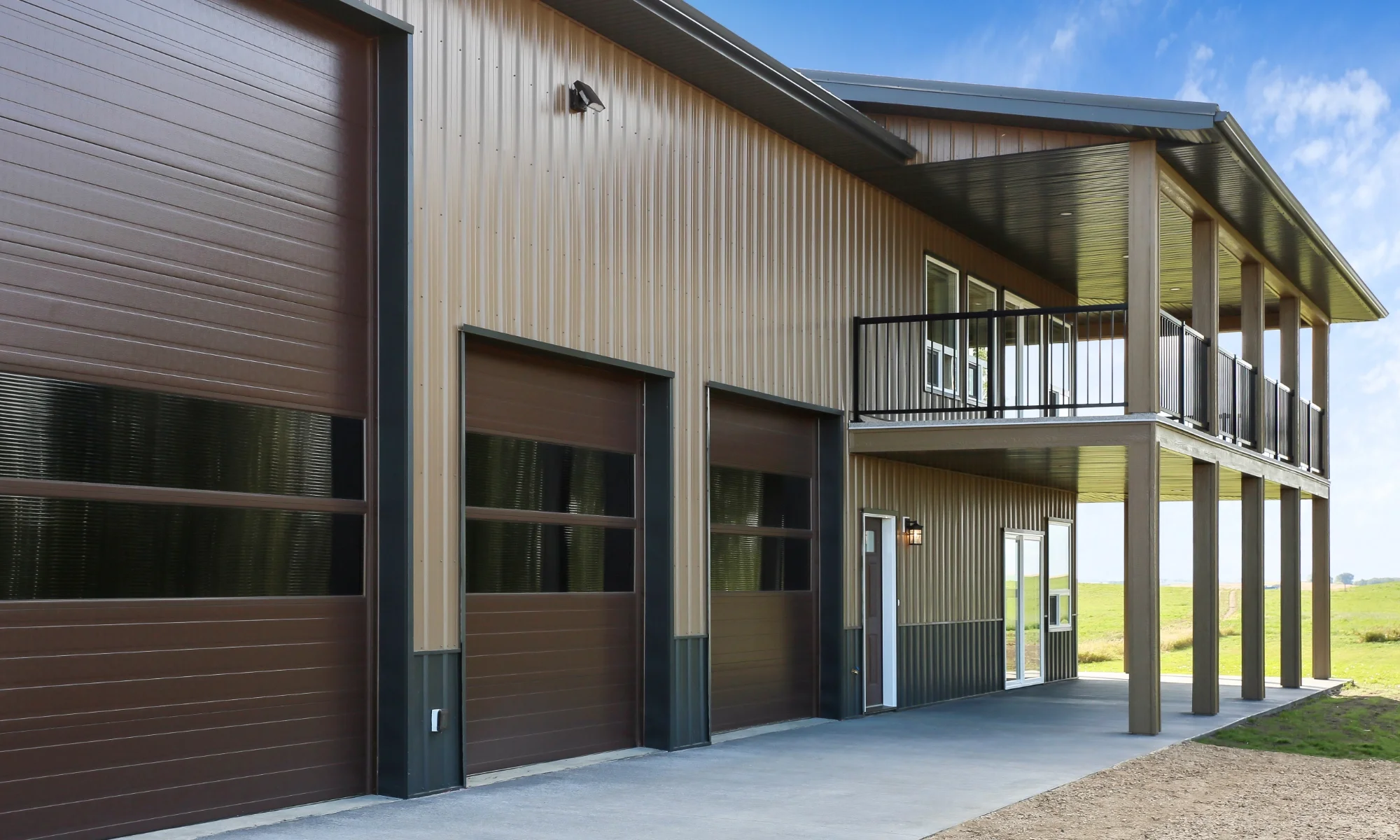 Two-Storey barndominium with upper balcony, modern metal siding, and integrated garage doors.