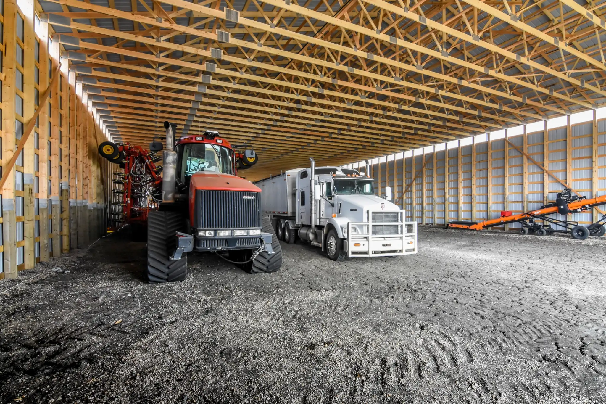 Several pieces of machinery and agricultural implements sit sheltered in a cold storage for farm equipment building.