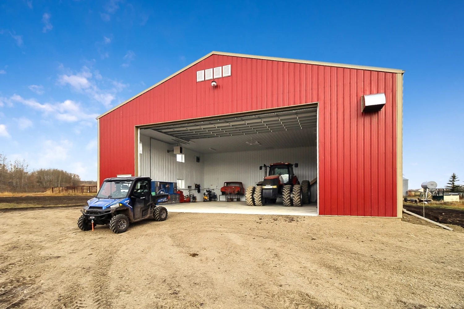 A red farm shop has many pieces of equipment parked in it and outside.
