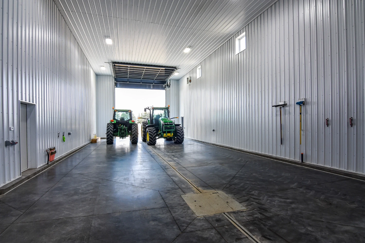 Two tractors sit inside a wash bay that is attached to a larger agricultural building.