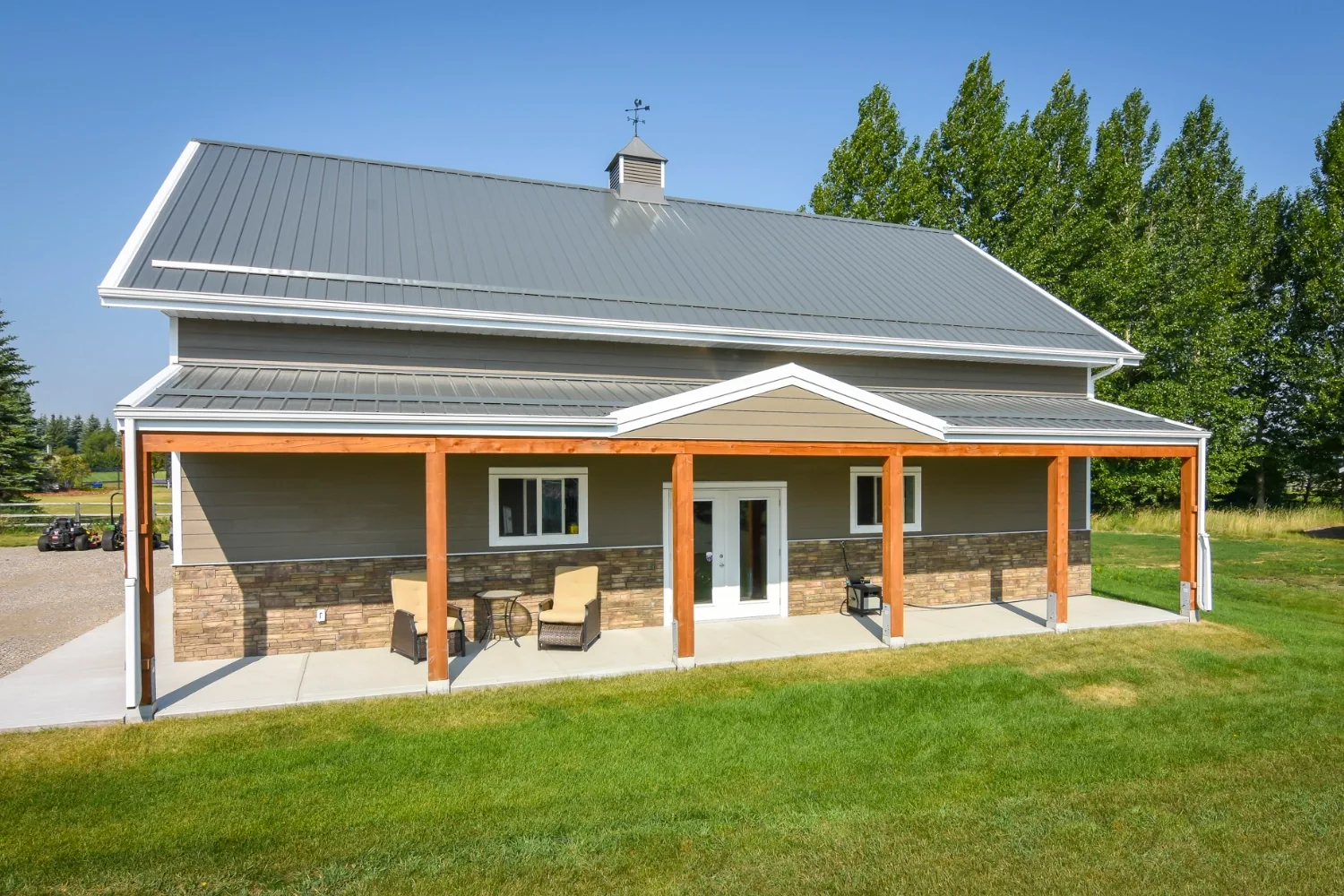 A lean to on an acreage post frame garage creates an outdoor porch. A mid-gable detail adds an elevated look.