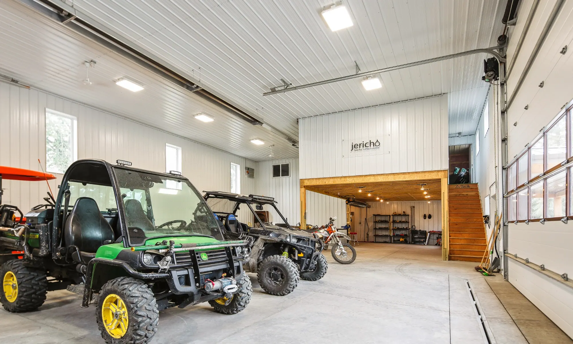 Fully finished shop interior of a pole barn building workshop with mezzanine for upper and lower-level storage solutions provides space for recreational vehicles on a concrete floor.