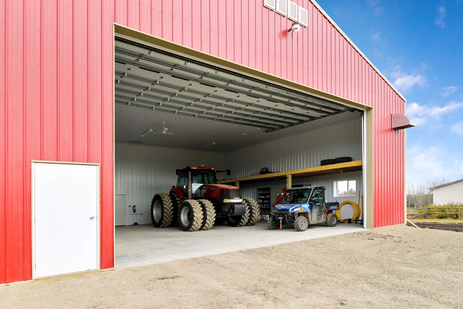 A farm shop building with the overhead door open to unveil the finished interior and several pieces of equipment.