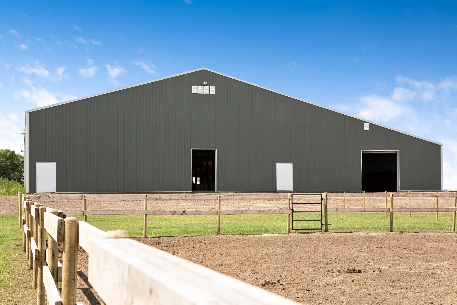 An indoor riding arena sits closely to outdoor pastures and pens for horses to facilitate easy riding.