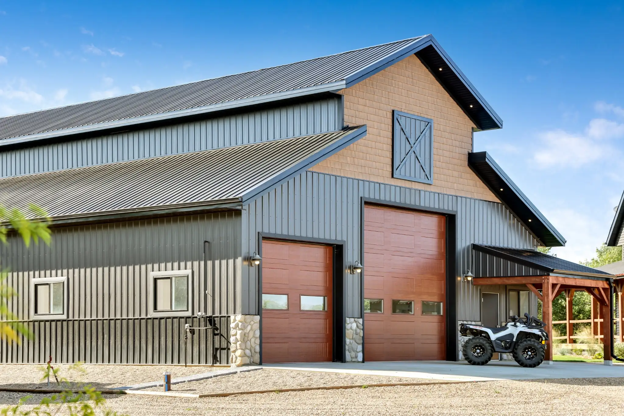 Stone wainscoting, a faux hay door, and a porch combine to create a polished appearance on a monitor-style workshop for an upscale acreage.