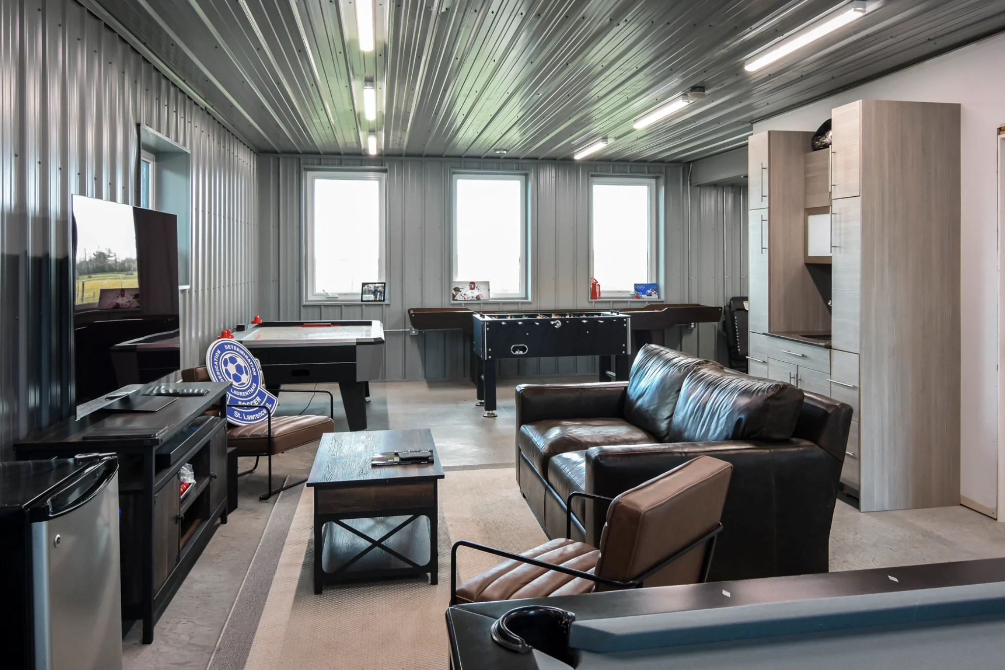 Lounge area inside a post frame building is finished with wall metal, and features games and a tv for relaxing.