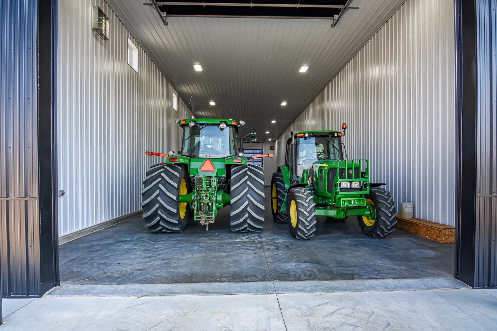 Two clean tractors sit inside a wash bay attached to an agricultural building.