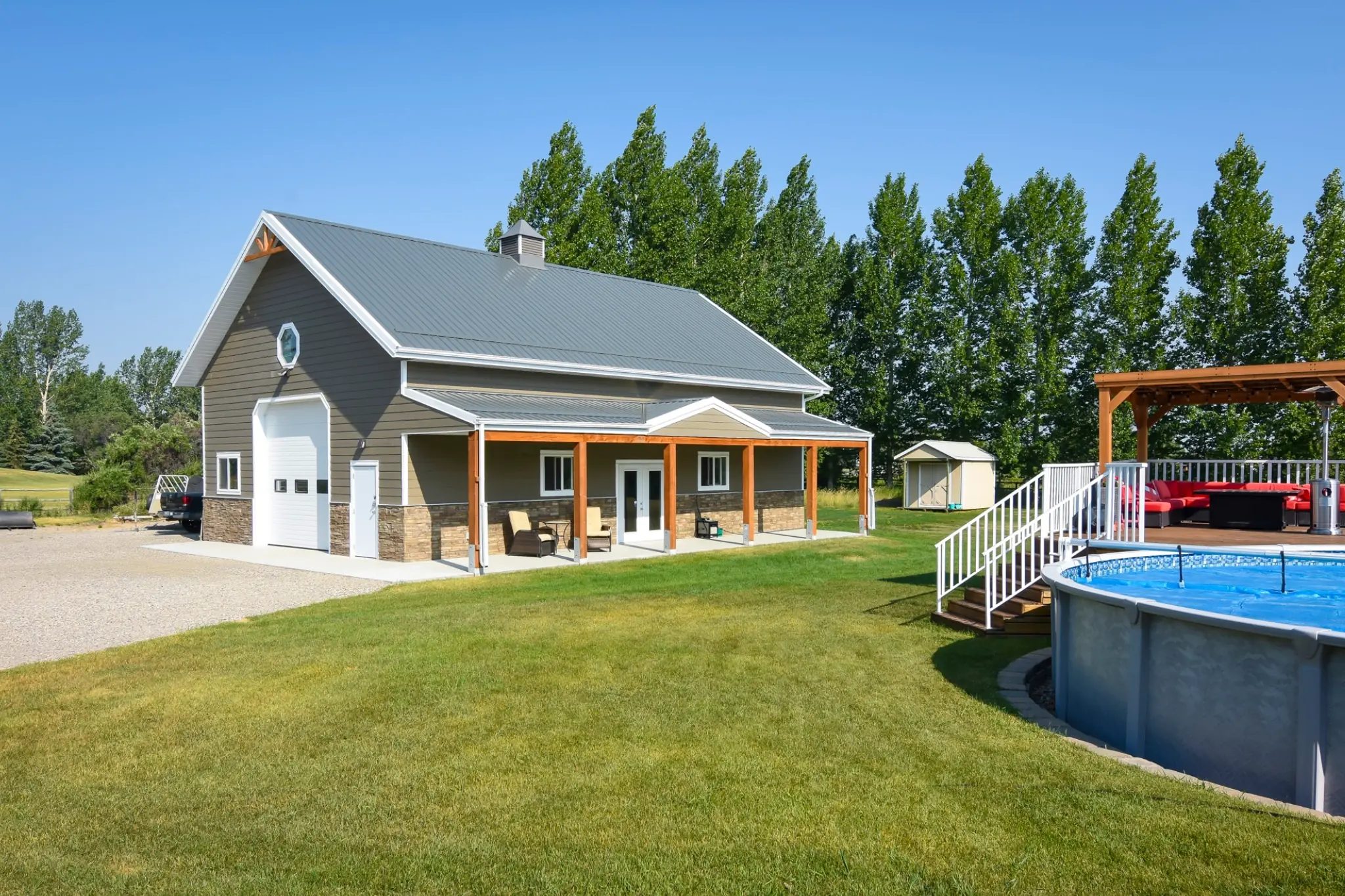 The covered outdoor porch space of a post frame garage faces an above ground pool—a perfect orientation for a family.