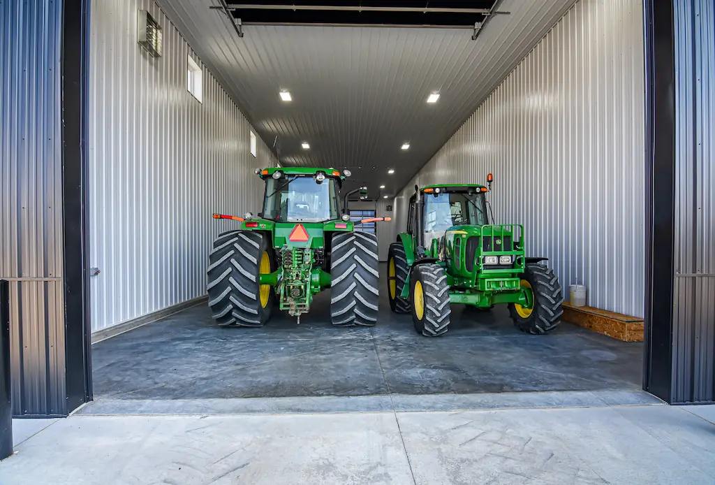 Farm equipment sits inside a post frame building with wash bay
