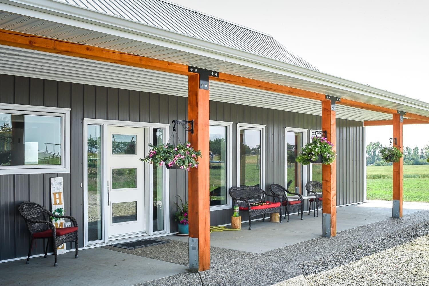 The front entrance of a post frame bungalow is covered by a roof supported with exposed posts and beams.