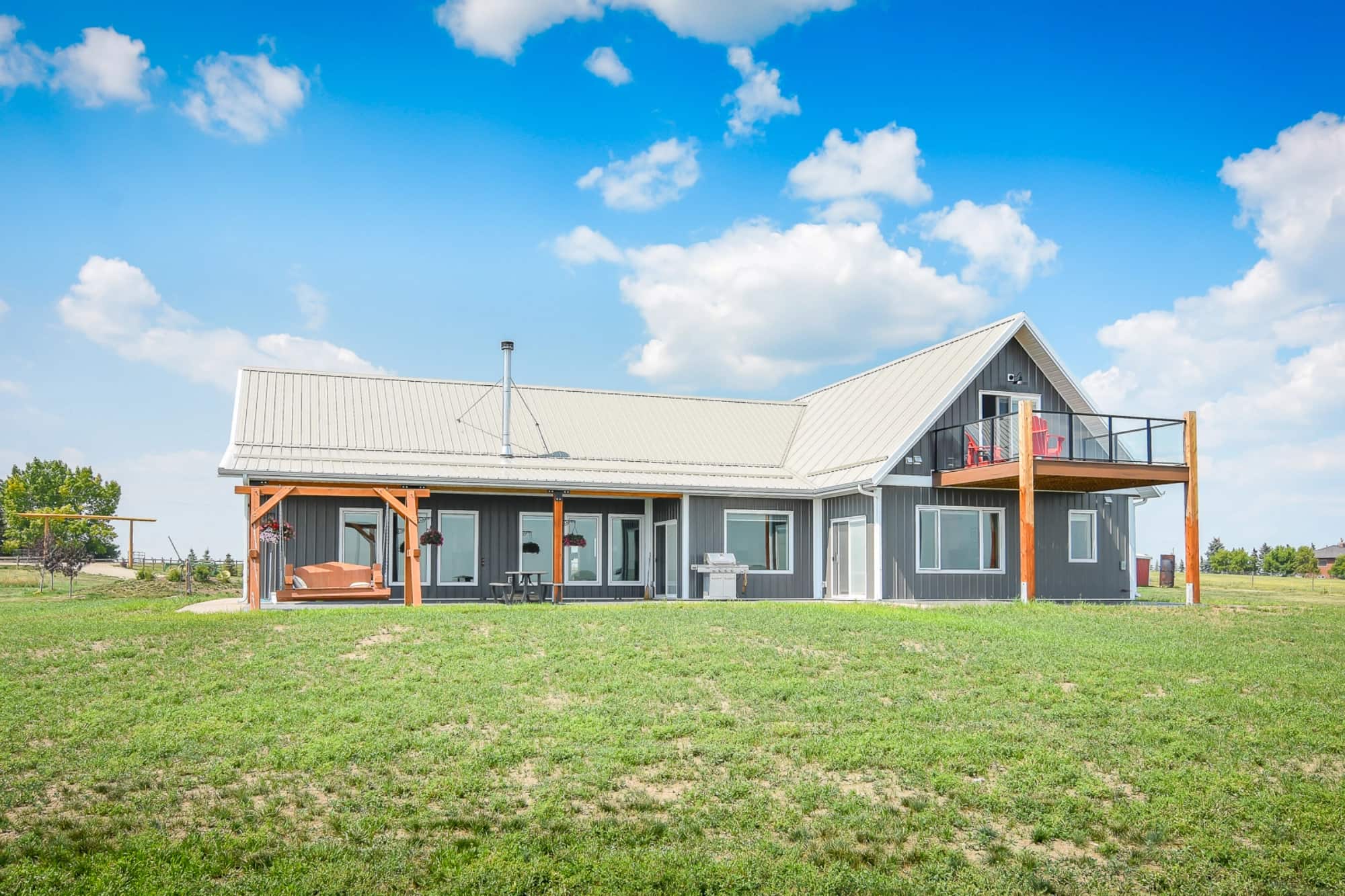 The back of a grey post frame home features multiple living spaces that look out over the scenic countryside.