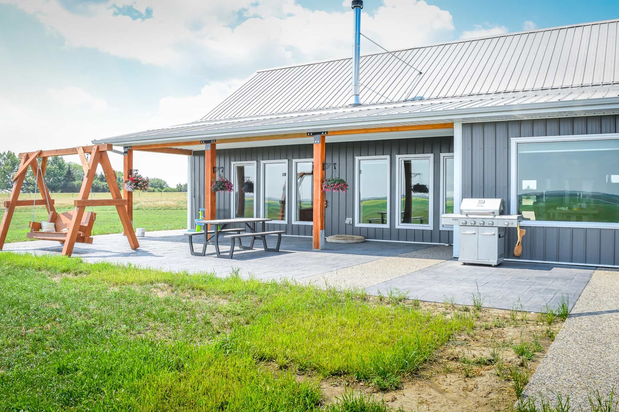 The back porch of a post frame bungalow is attached to the kitchen, and offers space a bbq and outdoor seating.