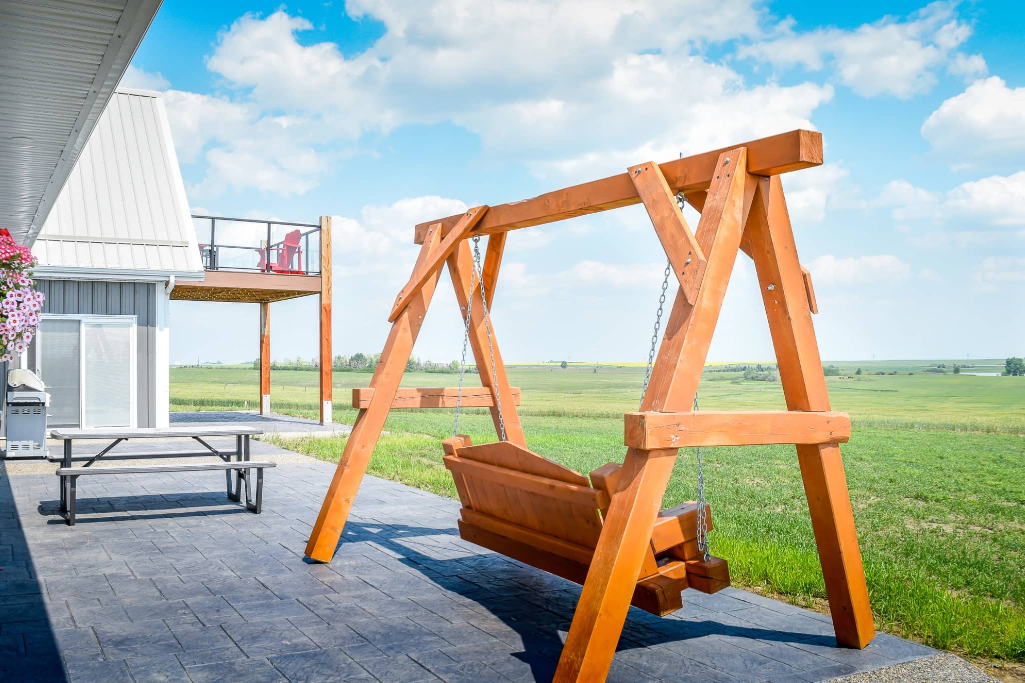 A porch swing looks out over the scenic, peaceful countryside behind a post frame home