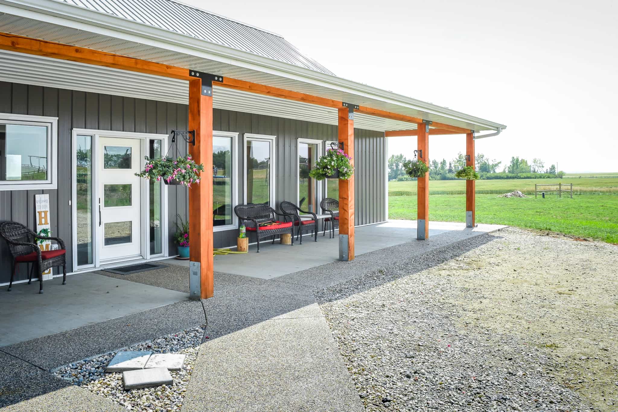 The front entrance of a post frame bungalow is covered by a roof supported with exposed posts and beams.