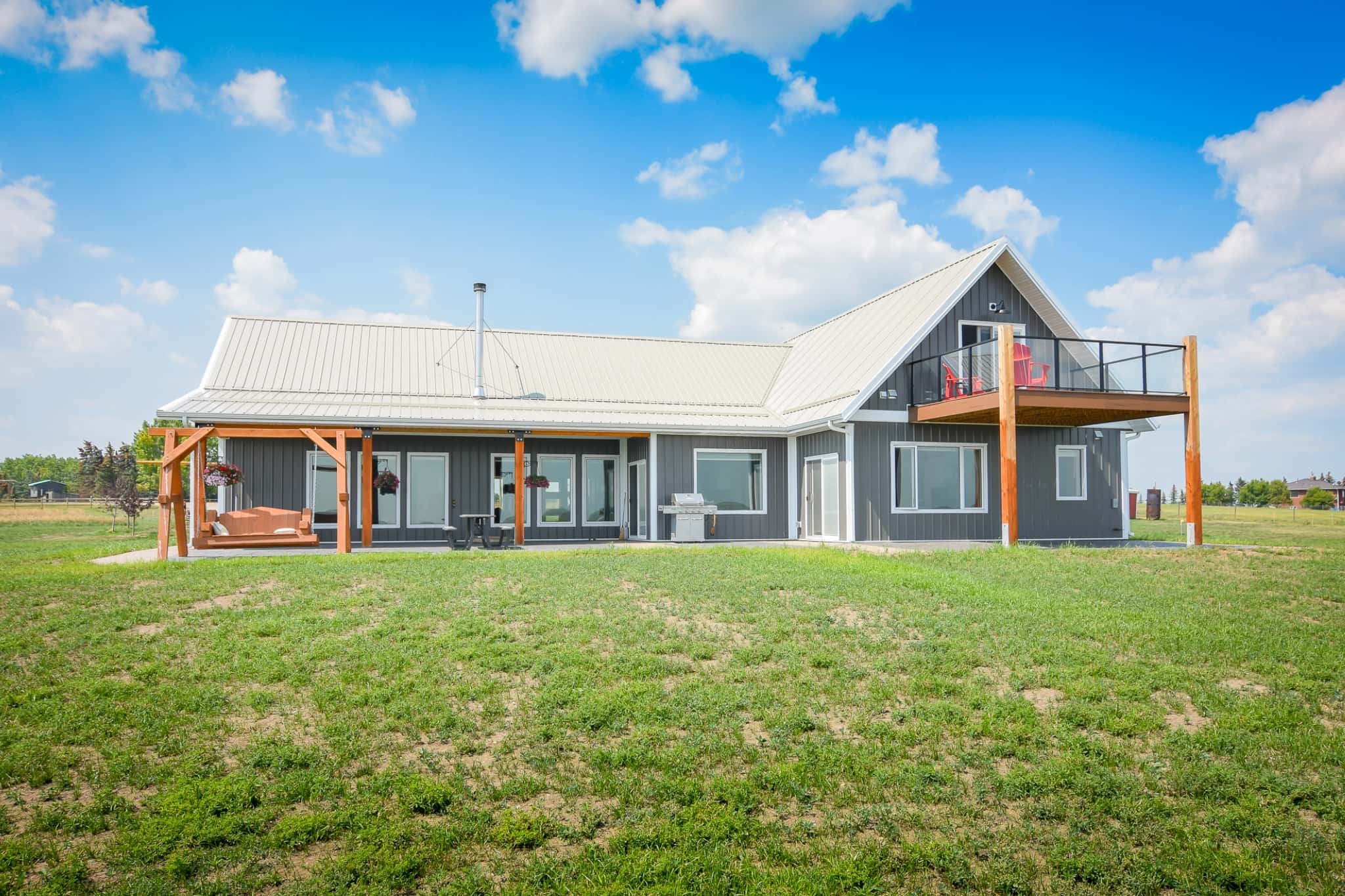 The back of a post frame bungalow overlooks the countryside.
