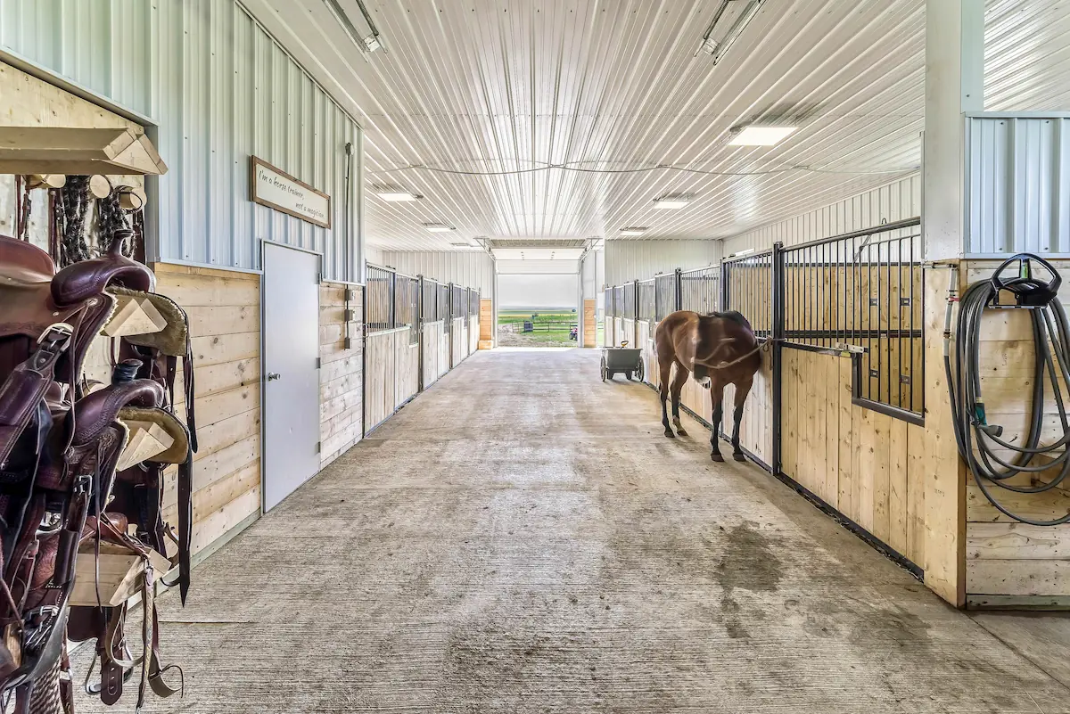 Interior of a fully finished horse barn with stalls, a kick wall, wash bay, and a tack room