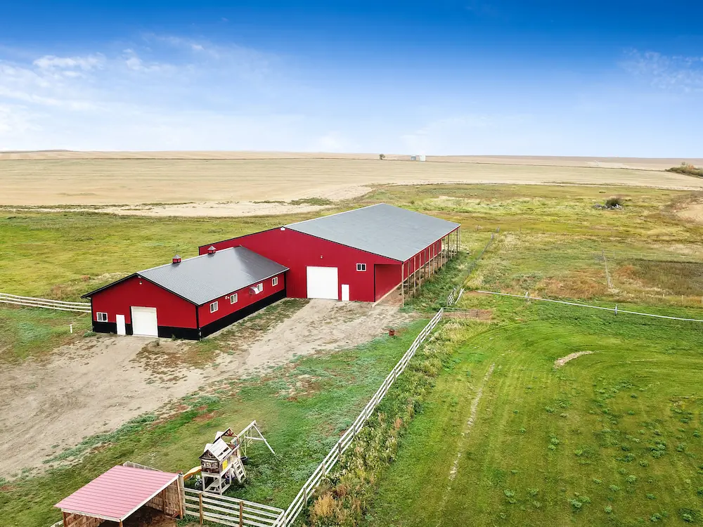 Exterior of a red and black horse barn with riding arena, combining to make the ultimate equestrian facility.