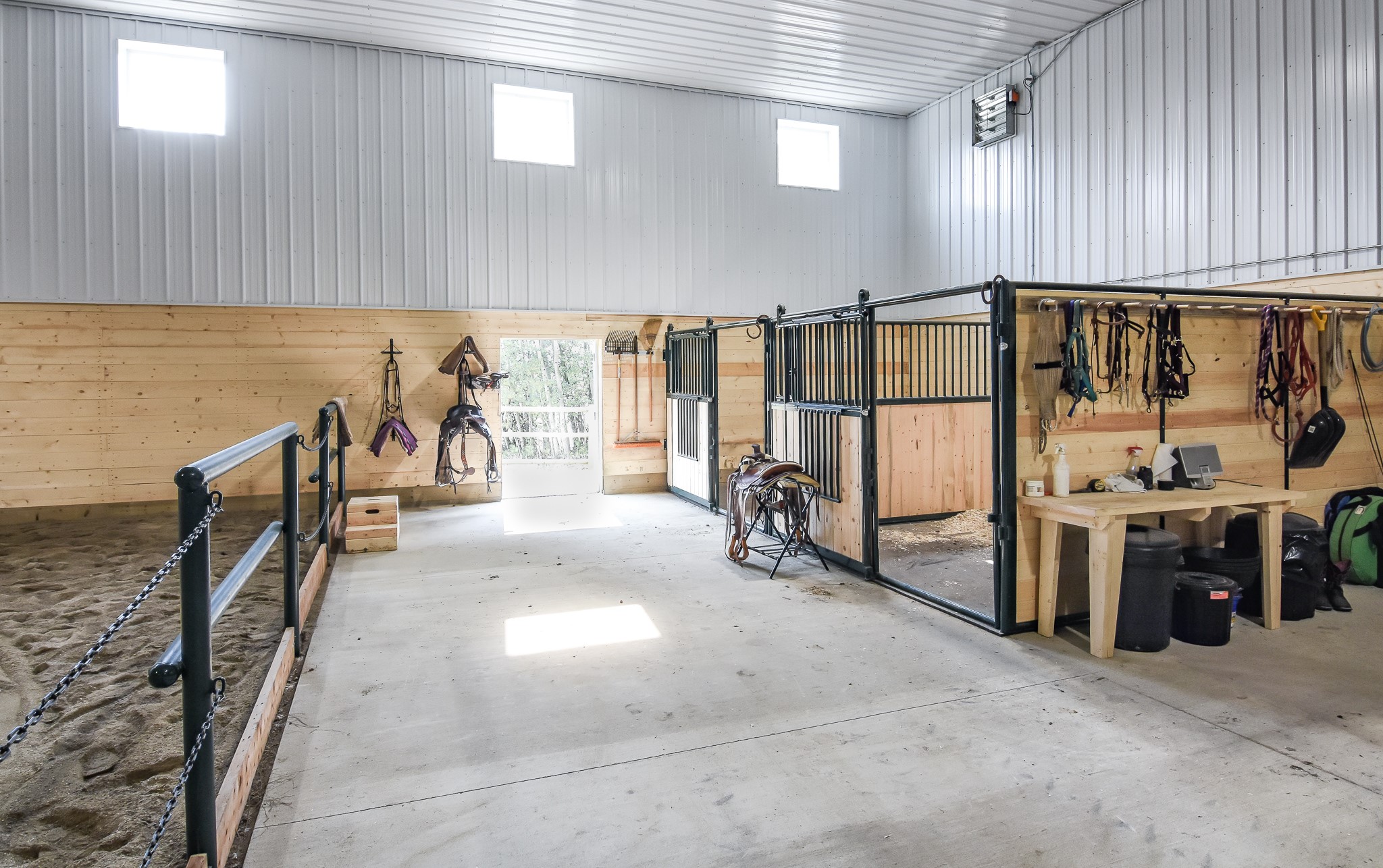 An indoor riding arena with horse stalls and other features to enhance comfort and safety, like exhaust fans.