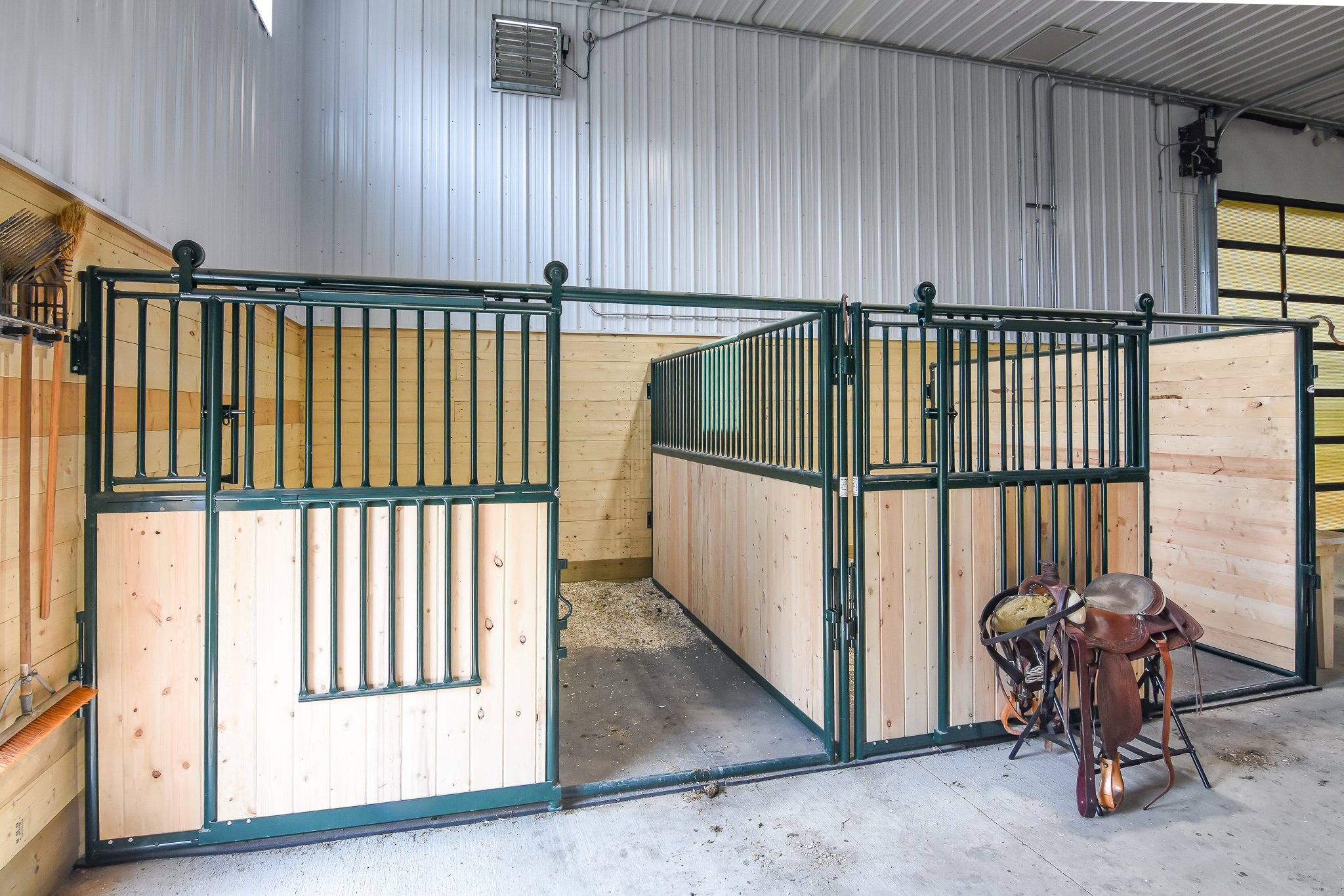 A riding arena that features two spacious, rustic horse stalls.