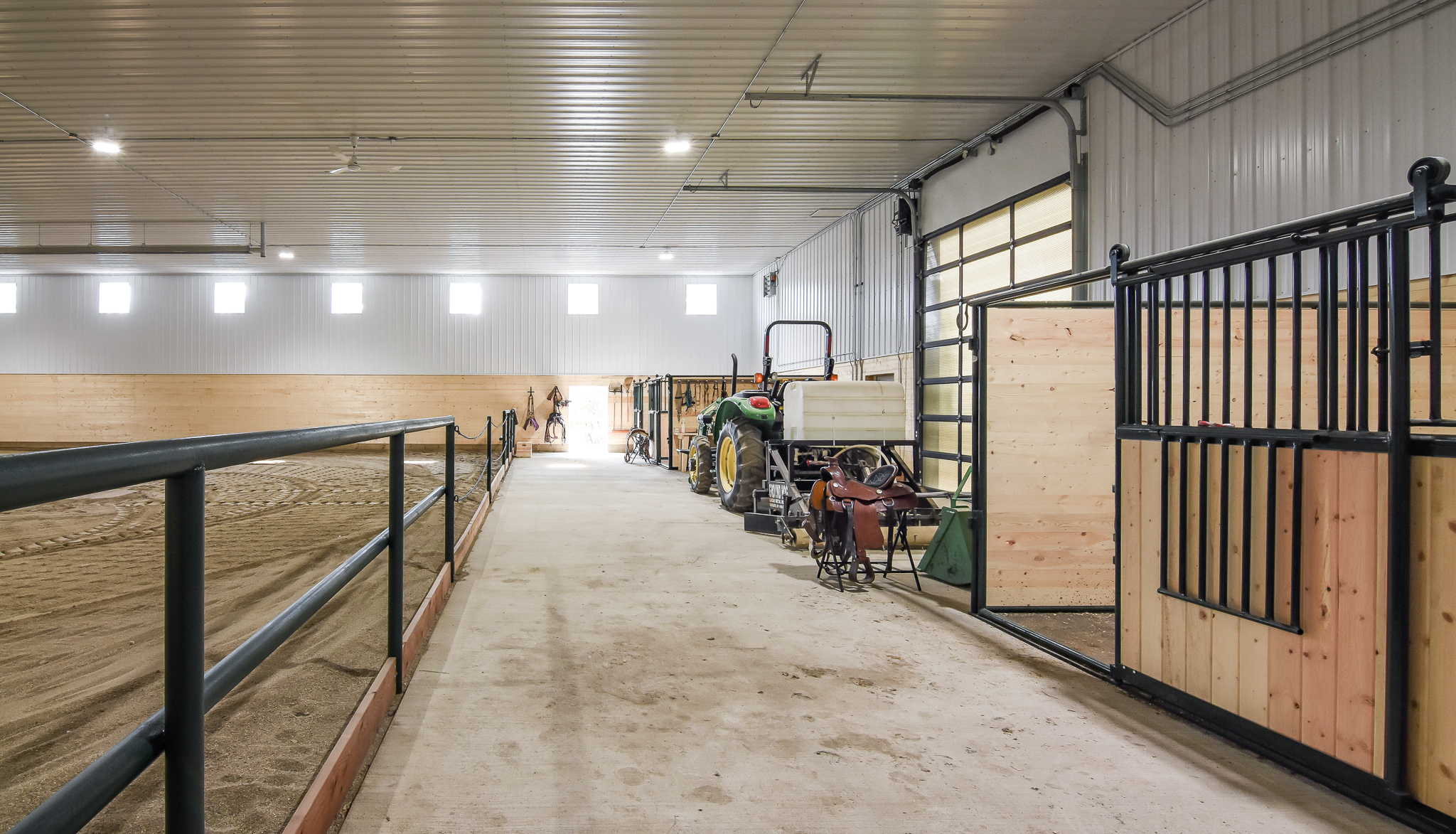 A multi-use area within a riding arena with horse stalls for loafing, equipment storage, viewing area, and space to saddle before riding.