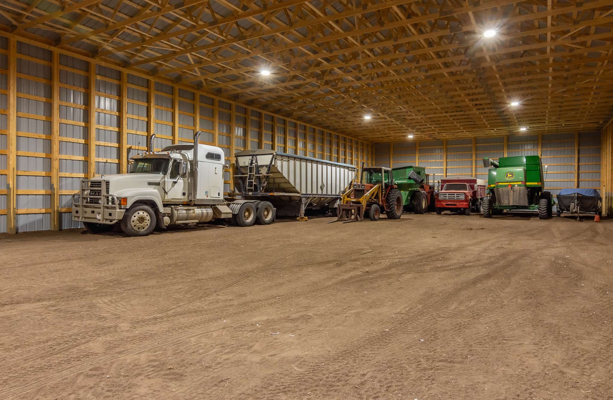 Trucks, a combine, and other farm implements inside a durable cold storage building for farm equipment