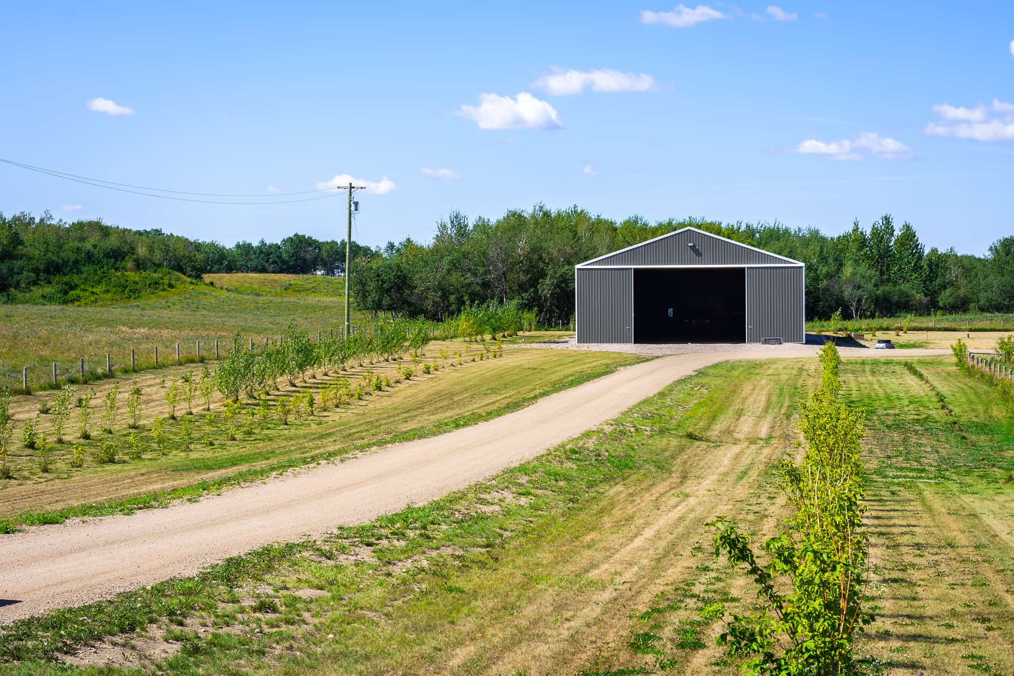 Post frame cold storage building on a rural Alberta farm, showcasing sable walls, bright white trim, and carbon steel roof designed for durable agricultural equipment storage.