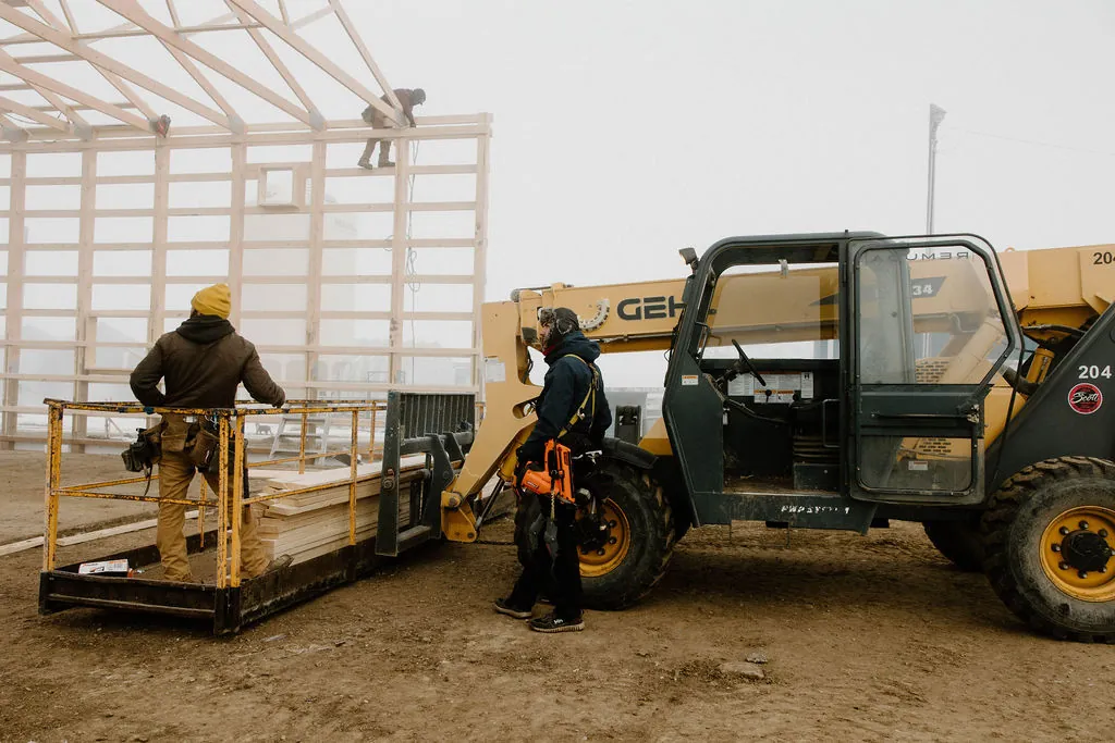 Post frame building being constructed during the Canadian winter, with workers and machinery in the foreground