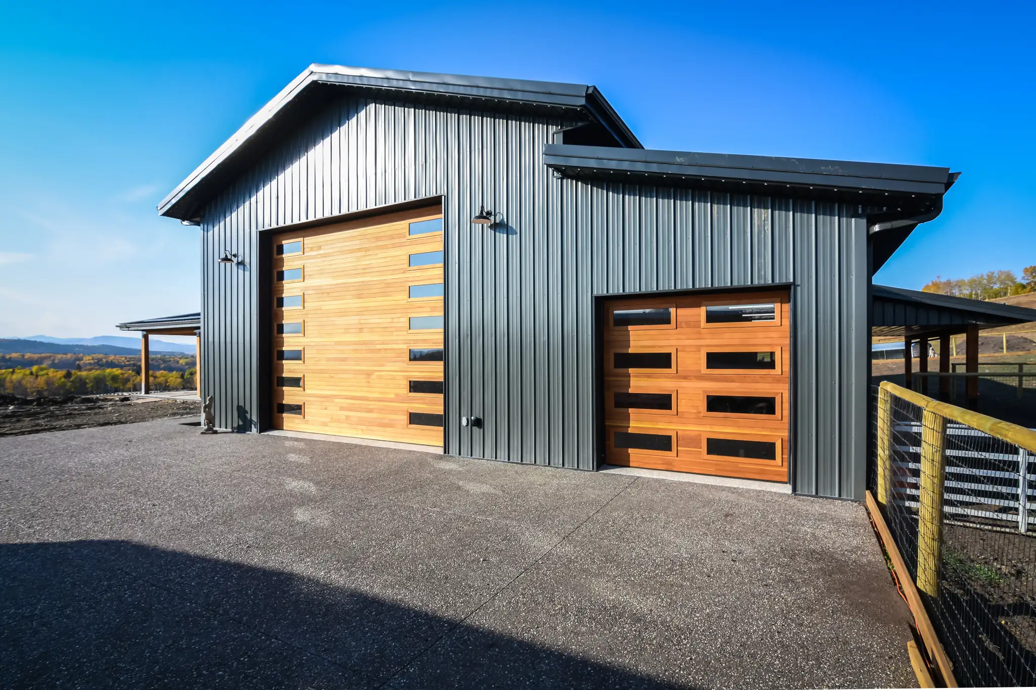 Garage and storage bays with wood-tone overhead doors connected to a small barndominium.