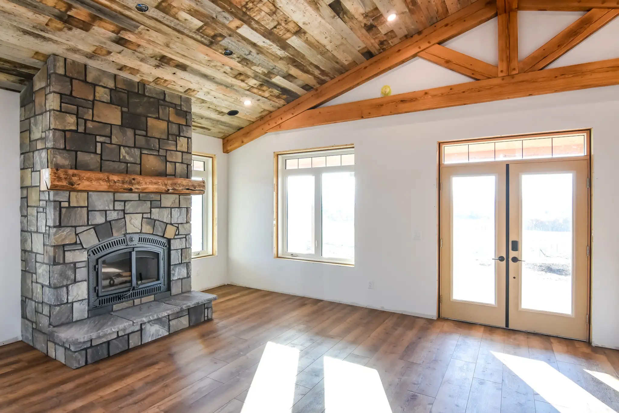 Wooden fireplace, large windows, and exposed timber detailing create a comfortable barndominium interior.