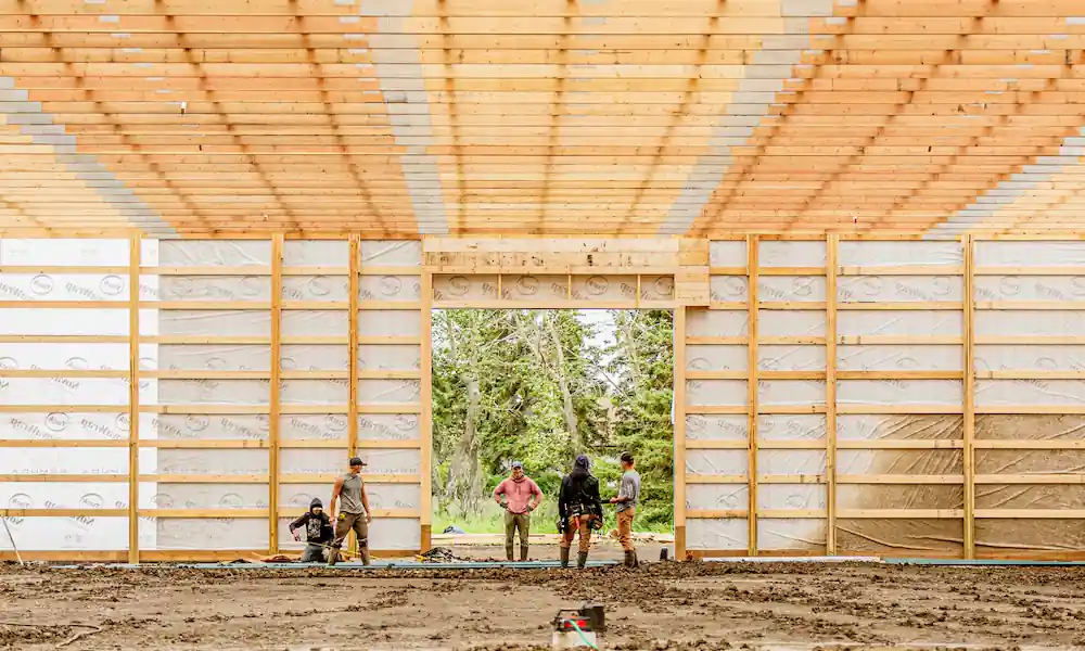 Post frame construction process in action, with crew members cutting metal cladding