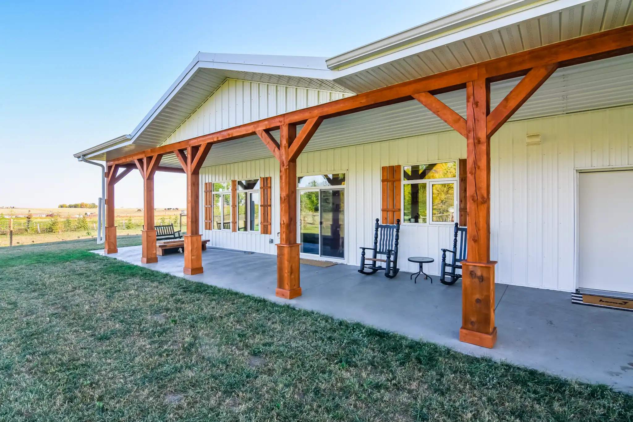 Covered porch on a white single story barndominium with exposed fir beams