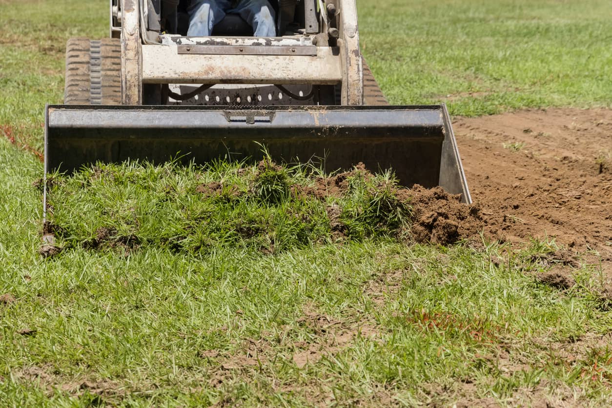 A skid steer stripping a site to prepare a building pad